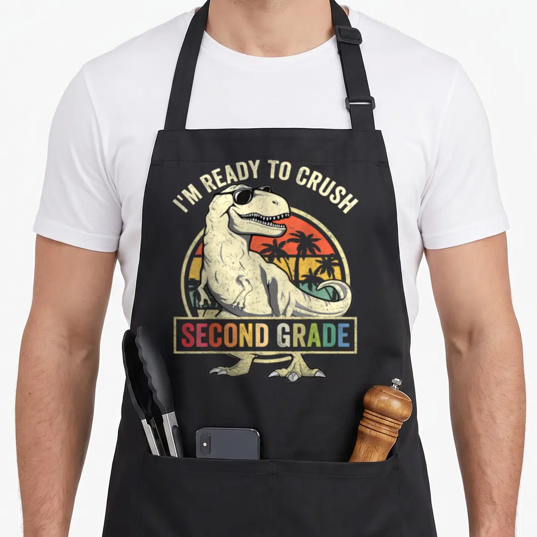 Crush 2nd apron - Retro T-Rex sunglasses retro sunset palm trees I'M READY TO CRUSH SECOND GRADE text banner — shown on a black cotton canvas apron against a white background