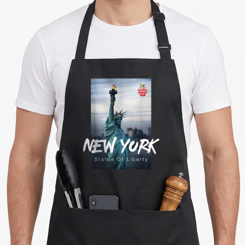 Funny statue new york apron - Statue of Liberty photo with NEW YORK text and red apple logo on black apron — shown on a black cotton canvas apron against a white background