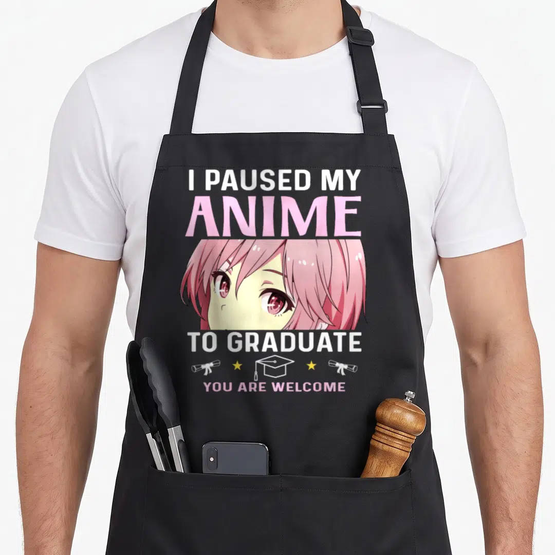 Graduation anime apron - I Paused My Anime To Graduate text above anime girl face with cap and diploma icons — shown on a black cotton canvas apron against a white background