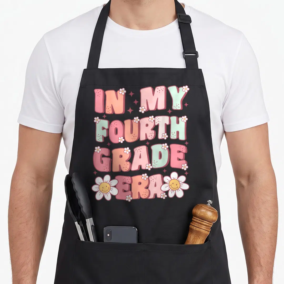 Fourth groovy grade apron - Stacked IN MY FOURTH GRADE ERA text with smiling daisies and pastel bubble letters — shown on a black cotton canvas apron against a white background