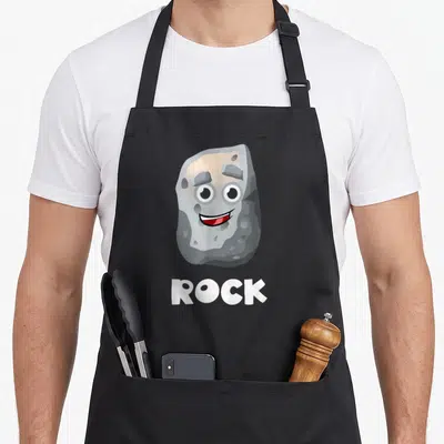 Halloween paper apron - Cartoon grey rock with face and white ROCK text below — shown on a black cotton canvas apron against a white background