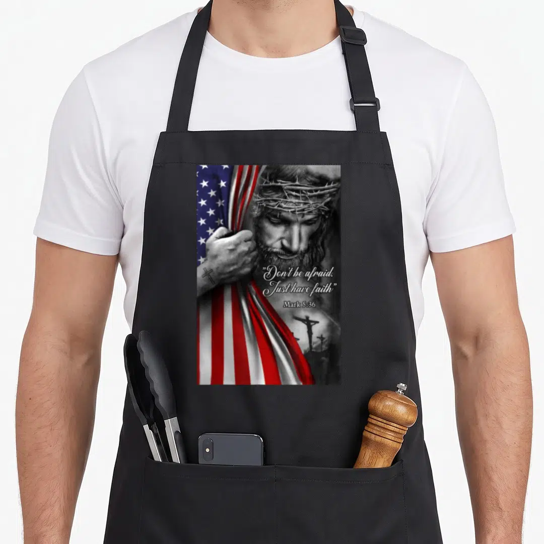 Afraid funny christian aprons - Jesus with crown of thorns holding red white and blue flag with scripture text — shown on a black cotton canvas apron against a white background