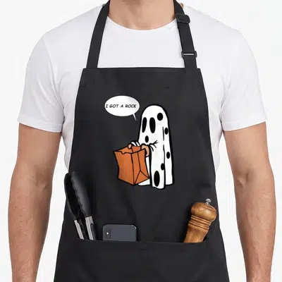 Rock ghost halloween apron - Cartoon ghost holding orange bag with speech bubble reading I Got A Rock — shown on a black cotton canvas apron against a white background