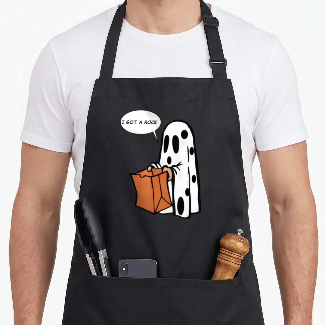 Rock ghost halloween apron - Cartoon ghost holding orange bag with speech bubble reading I Got A Rock — shown on a black cotton canvas apron against a white background