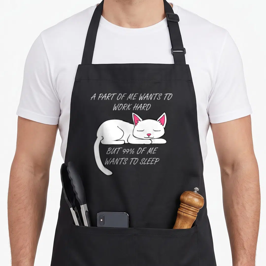 Office kitty cat apron - Sleeping white cartoon cat with pink ears and text about wanting to sleep instead of working — shown on a black cotton canvas apron against a white background