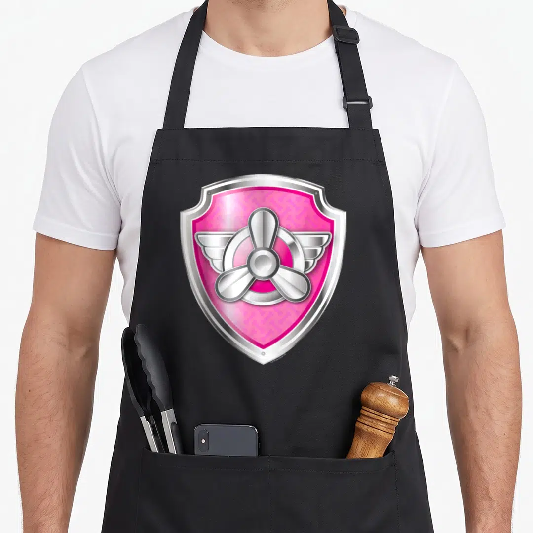 Badge isle of skye apron - Pink shield with silver propeller and wings in cartoon style — shown on a black cotton canvas apron against a white background