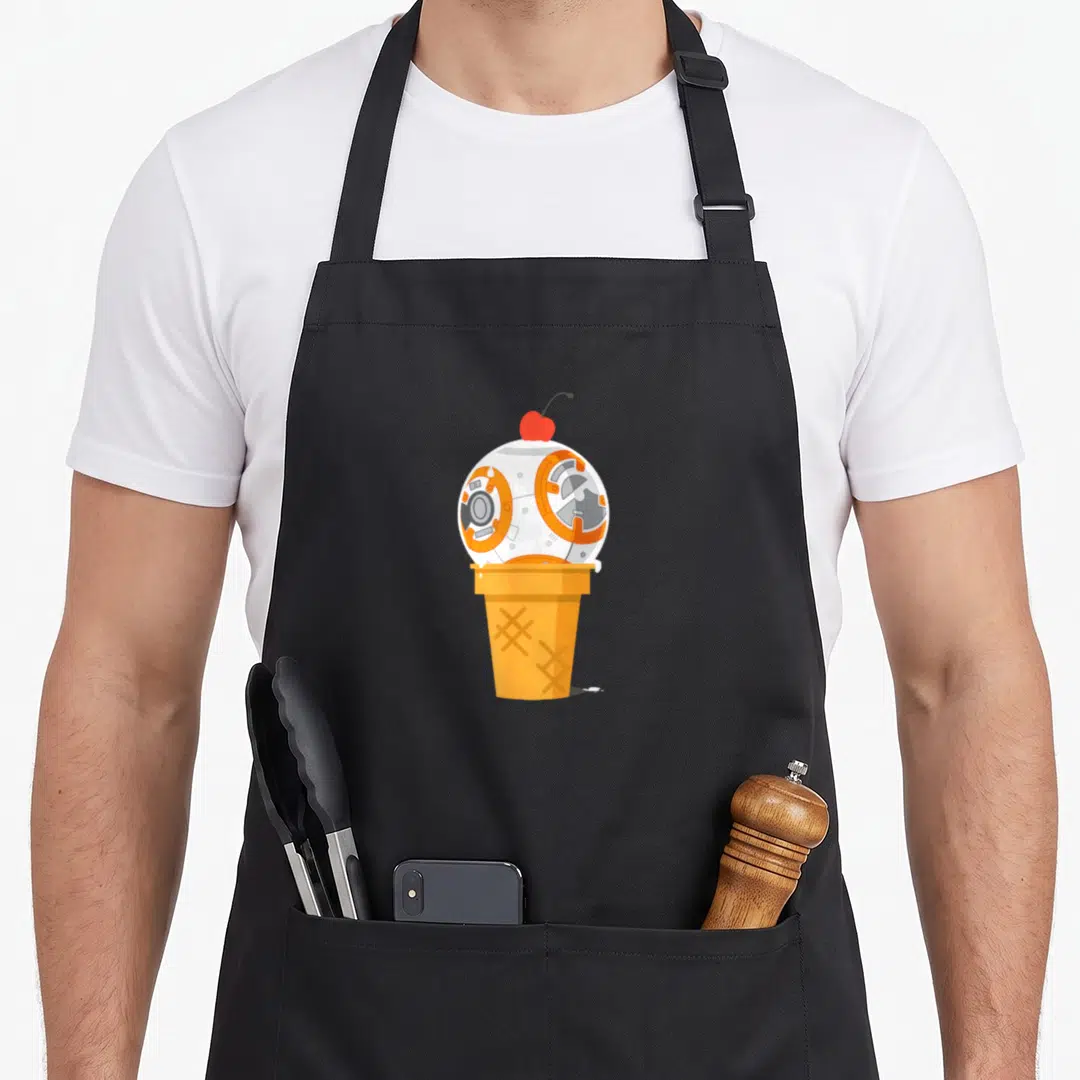 Cute ice cream apron - Cartoon BB-8 droid head as ice cream scoop on waffle cone with red cherry — shown on a black cotton canvas apron against a white background