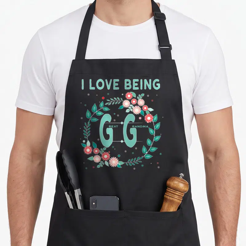 Gigi grandmother apron - Mint green I Love Being Great Grandma text inside a red and pink flower wreath — shown on a black cotton canvas apron against a white background