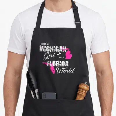 Michigan florida pride apron - Pink state maps of Michigan and Florida overlapping white stacked text with two small — shown on a black cotton canvas apron against a white background