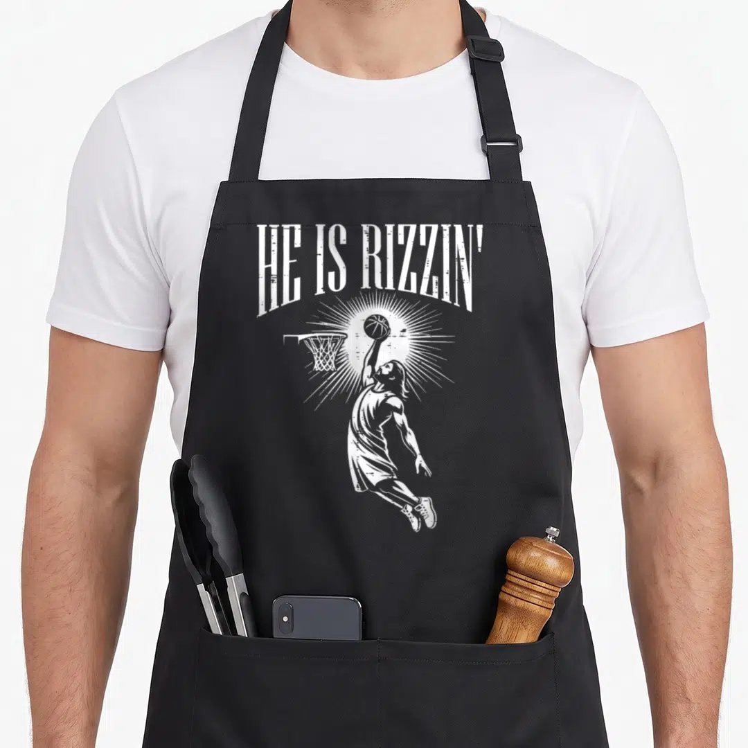 Rizzin easter apron - White distressed HE IS RIZZIN text above jumping basketball player with sunburst — shown on a black cotton canvas apron against a white background