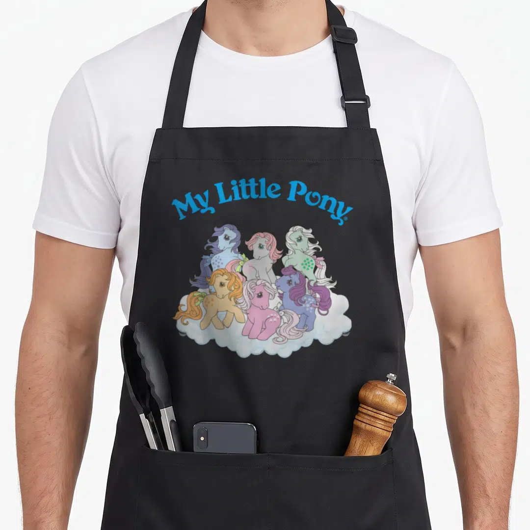 Original pony apron - My Little Pony text over six colorful ponies standing on a white cloud in cartoon style — shown on a black cotton canvas apron against a white background