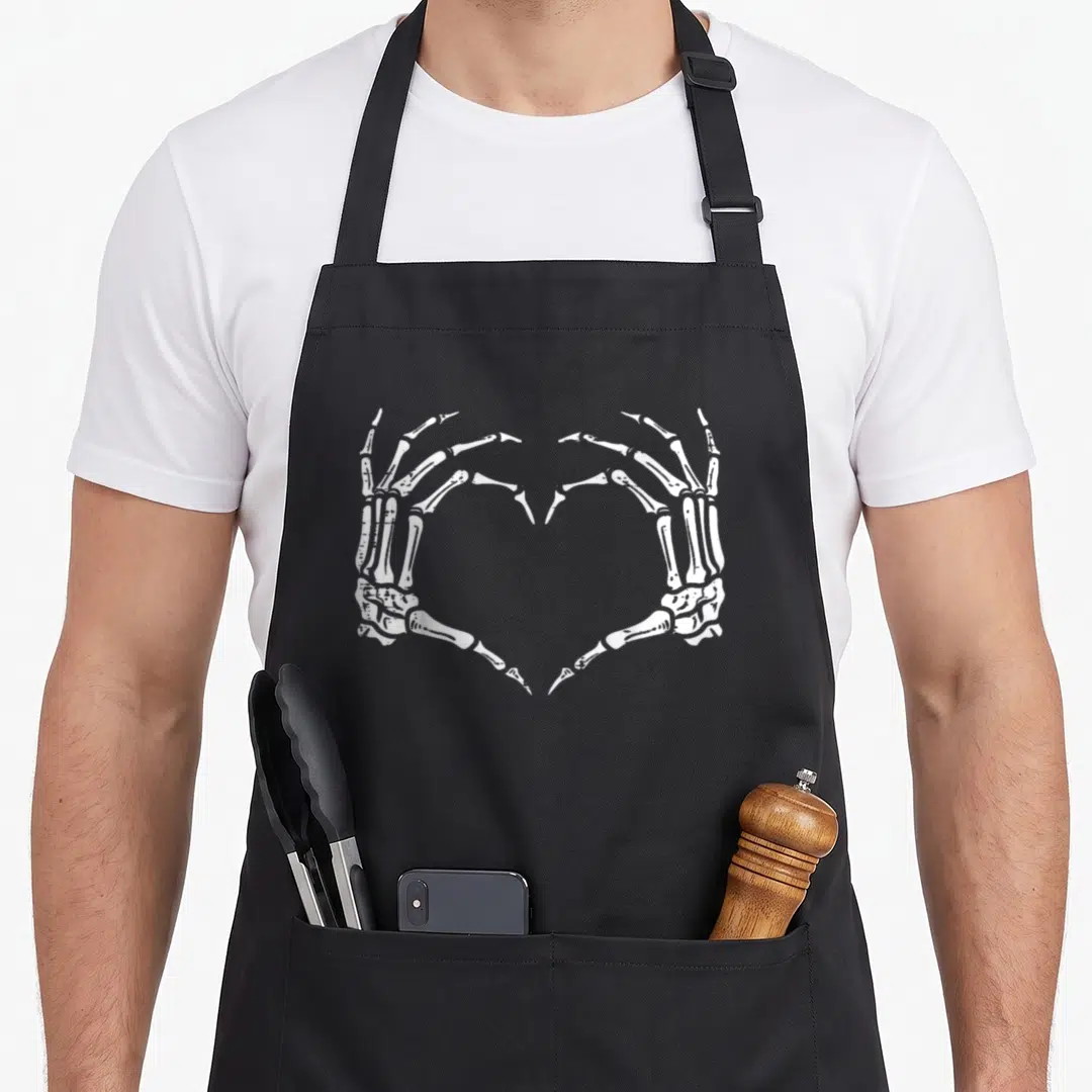 Sign skeleton apron - White skeletal hands forming a heart shape in line art on black fabric — shown on a black cotton canvas apron against a white background
