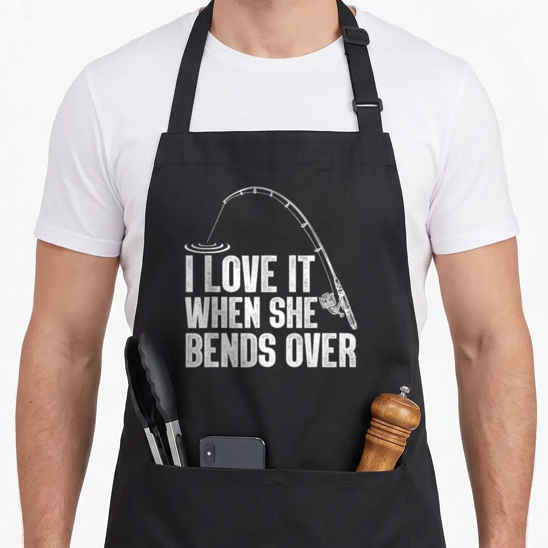 Fisherman rod fishing aprons - White distressed text I LOVE IT WHEN SHE BENDS OVER with bent fishing rod and water — shown on a black cotton canvas apron against a white background