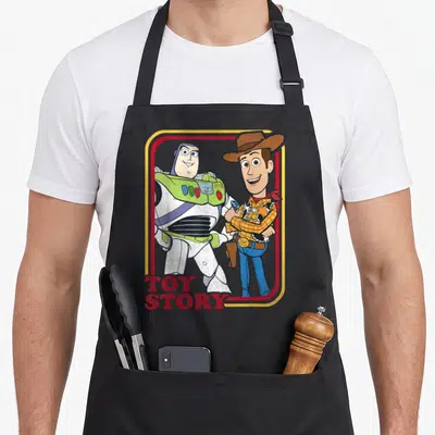 Woody camping apron - Cartoon Buzz Lightyear and Woody standing in red yellow frame with TOY STORY text — shown on a black cotton canvas apron against a white background