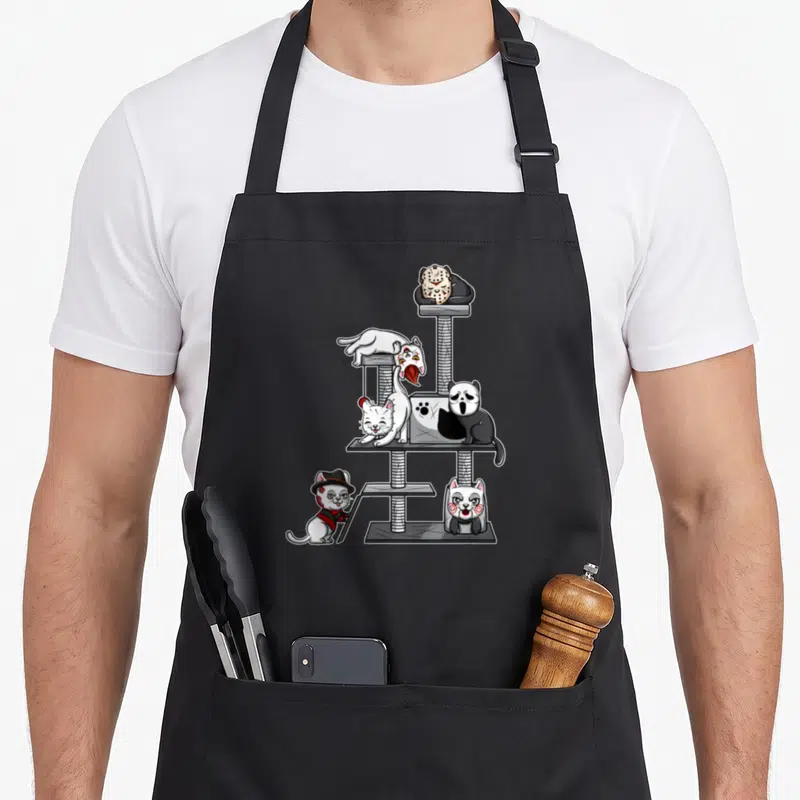 Horror cute cat apron - Five cartoon cats in horror costumes on a grey cat tree in white, grey, and black — shown on a black cotton canvas apron against a white background