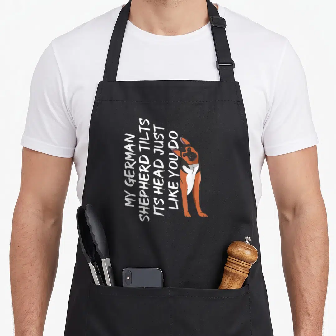 German tilt apron - Stacked white text next to a realistic tan black and white German Shepherd tilting its head — shown on a black cotton canvas apron against a white background