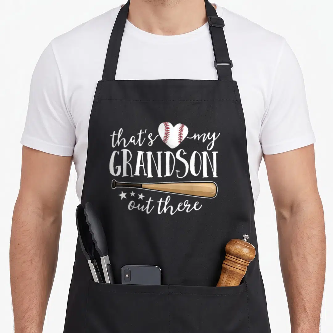 Grandson grandma apron - Heart baseball and tan bat with text that's my GRANDSON out there — shown on a black cotton canvas apron against a white background
