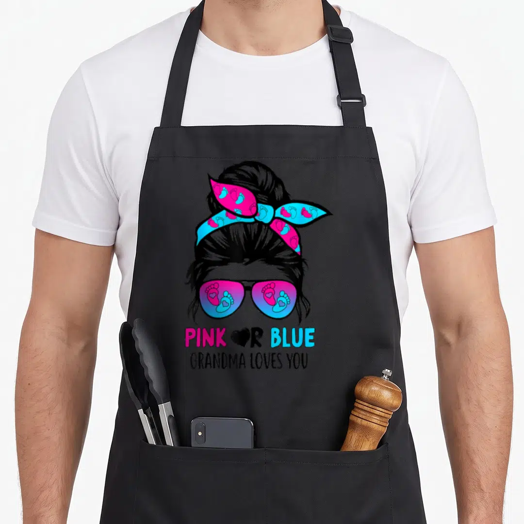 Messy grandma apron - Cartoon woman with bun and sunglasses containing pink and blue footprints with text PINK OR BLUE — shown on a black cotton canvas apron against a white background