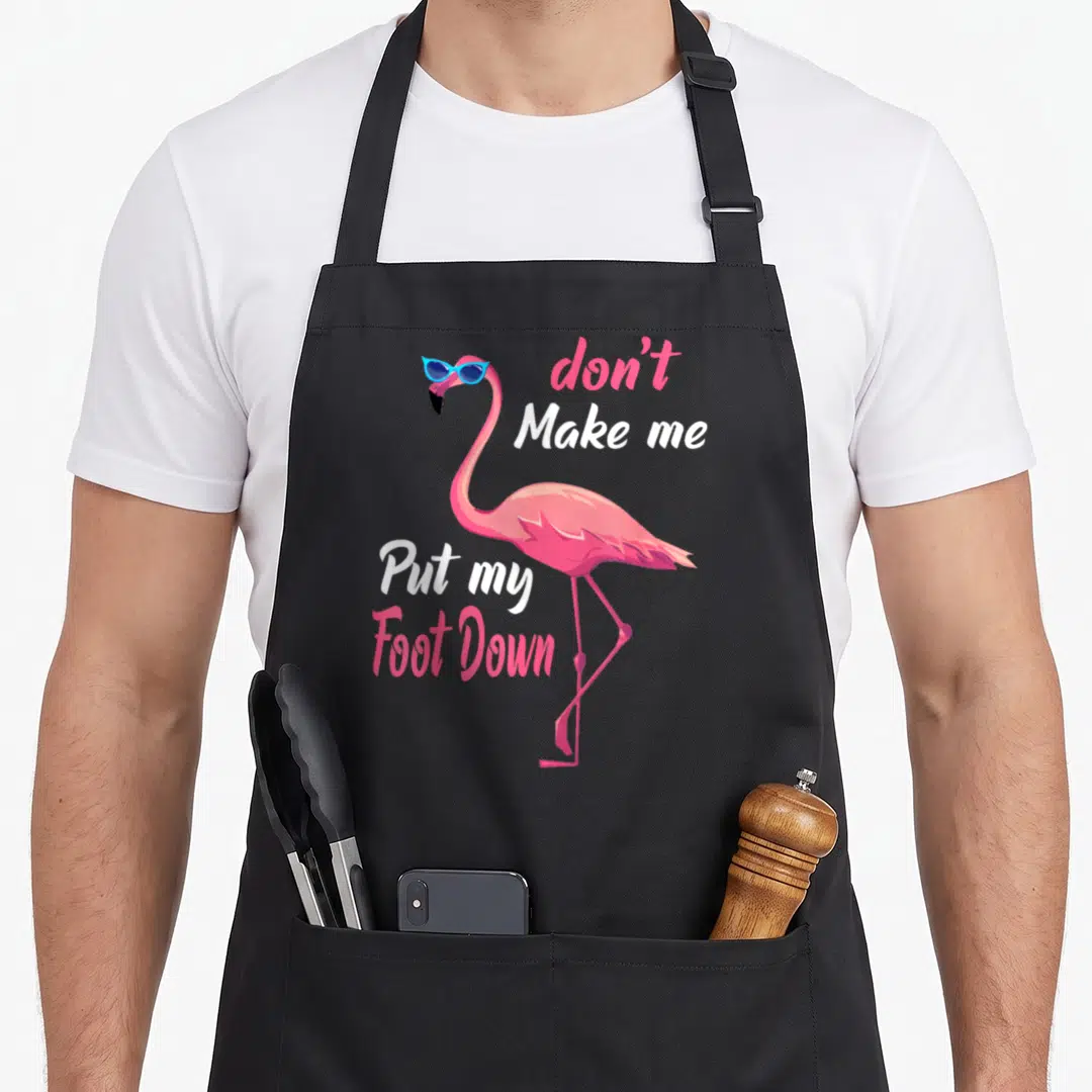 Awareness pink flamingo apron - Cartoon pink flamingo in blue sunglasses with text don't Make me Put my Foot Down — shown on a black cotton canvas apron against a white background