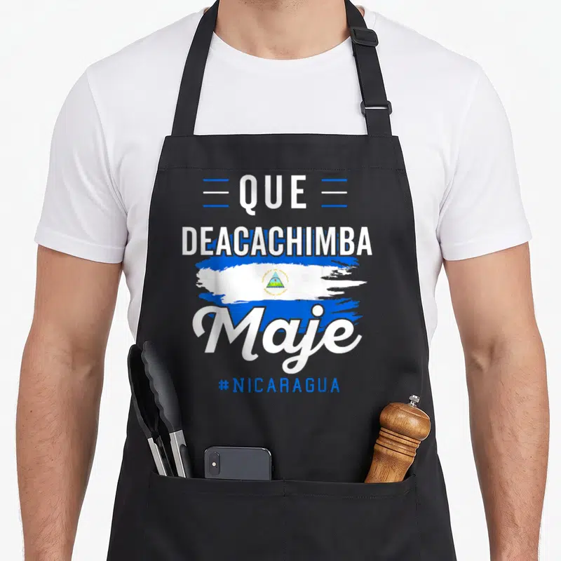 Camiseta nicaraguan girl apron - Stacked Que Deacachimba Maje text with distressed blue white flag brushstroke — shown on a black cotton canvas apron against a white background