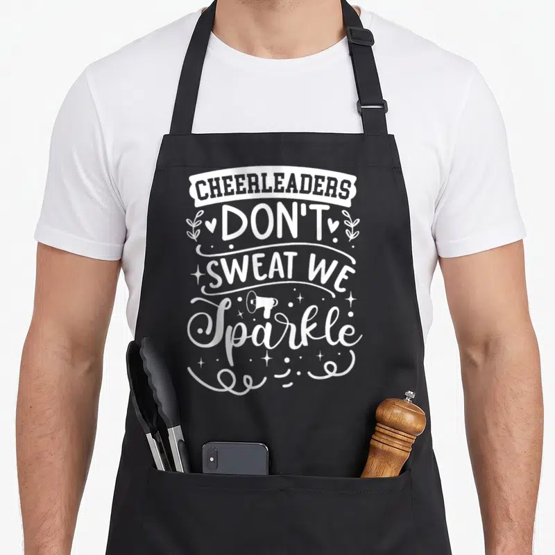 Cheerleader sweat apron - White stacked text reading CHEERLEADERS DON'T SWEAT WE Sparkle with megaphone and decorative — shown on a black cotton canvas apron against a white background