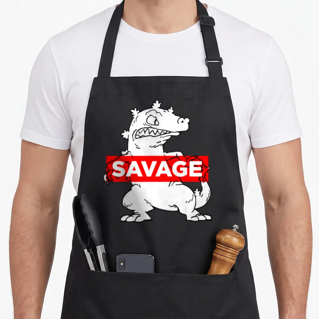 Reptar savage apron - White cartoon monster with red SAVANGE banner on black apron — shown on a black cotton canvas apron against a white background