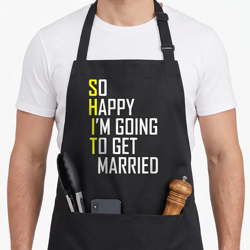 Wedding bride and groom apron - Stacked white text with yellow S H I T initials spelling vertically on stiff canvas — shown on a black cotton canvas apron against a white background