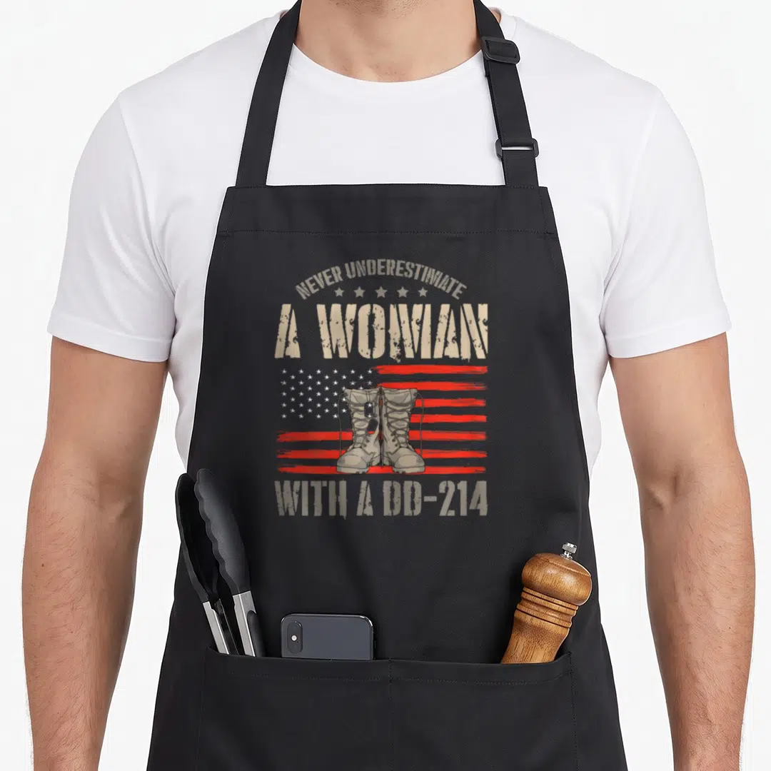 Funny female veteran apron - Combat boots over distressed flag with Never Underestimate A Woman With A DD-214 text — shown on a black cotton canvas apron against a white background