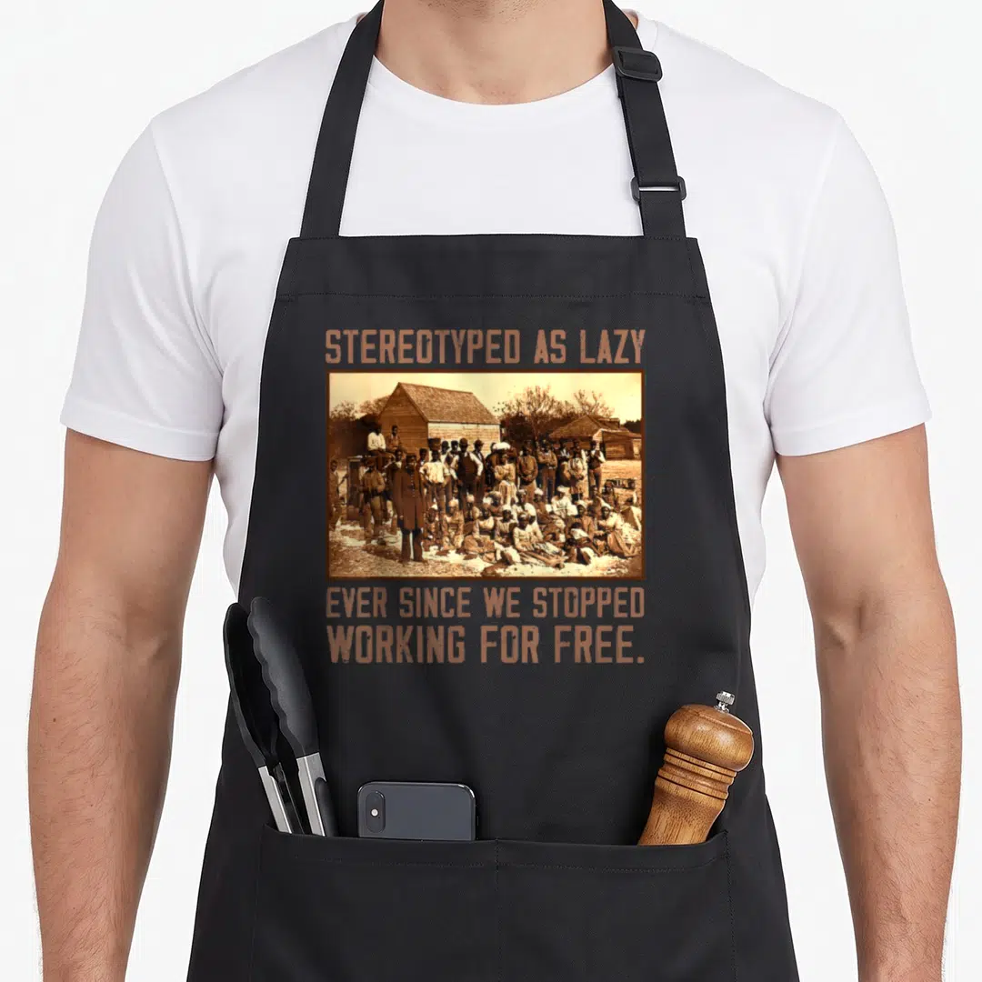 Stereotyped a's aprons - Sepia group photo with orange text stereotyped as lazy ever since we stopped working for free — shown on a black cotton canvas apron against a white background
