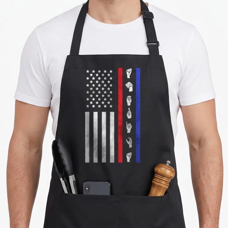 Asl american flag apron - Distressed flag with white stars and seven hand signs between red and blue stripes — shown on a black cotton canvas apron against a white background