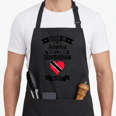 Trinidad tobago trinidadian boy apron - Text BORN IN America with a TRINIDADIAN HEART above red white and black heart — shown on a black cotton canvas apron against a white background