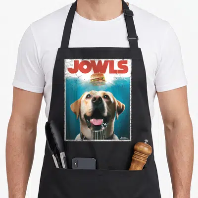 Lab jowl labrador apron - Photo of yellow lab looking up at floating burger under red JOWLS text with distressed white — shown on a black cotton canvas apron against a white background