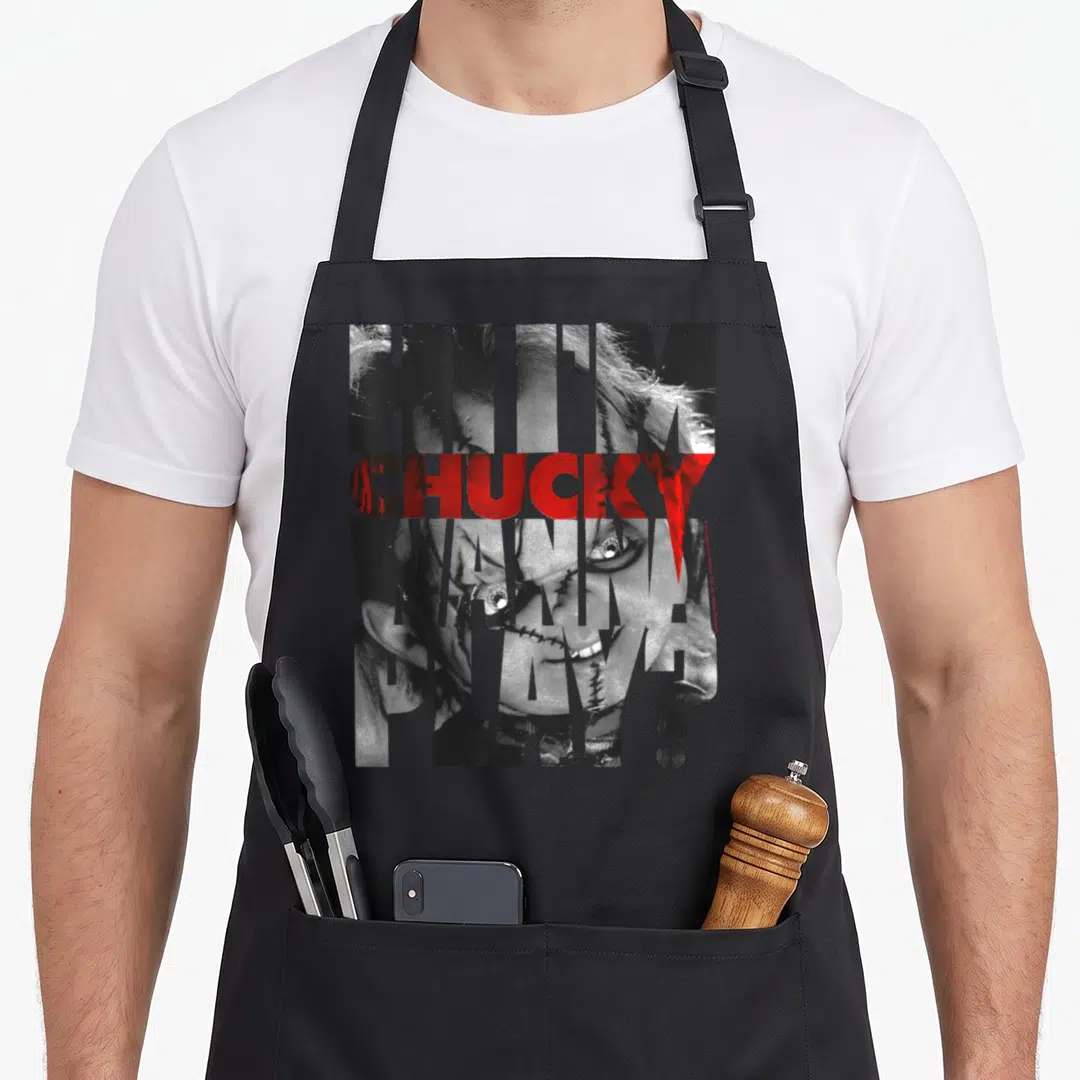 Play big brother apron - Stacked HI I'M CHUCKY WANNA PLAY text filled with grayscale doll face photo, red CHUCKY — shown on a black cotton canvas apron against a white background