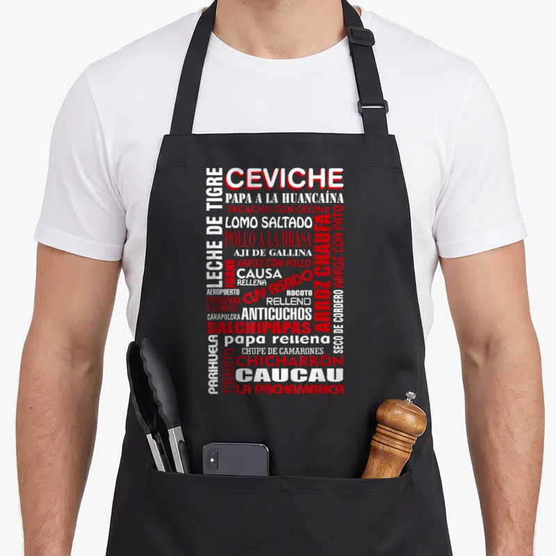 Peruvian golden apron - Red and white word cloud of Peruvian dish names including Ceviche and Lomo Saltado on black — shown on a black cotton canvas apron against a white background