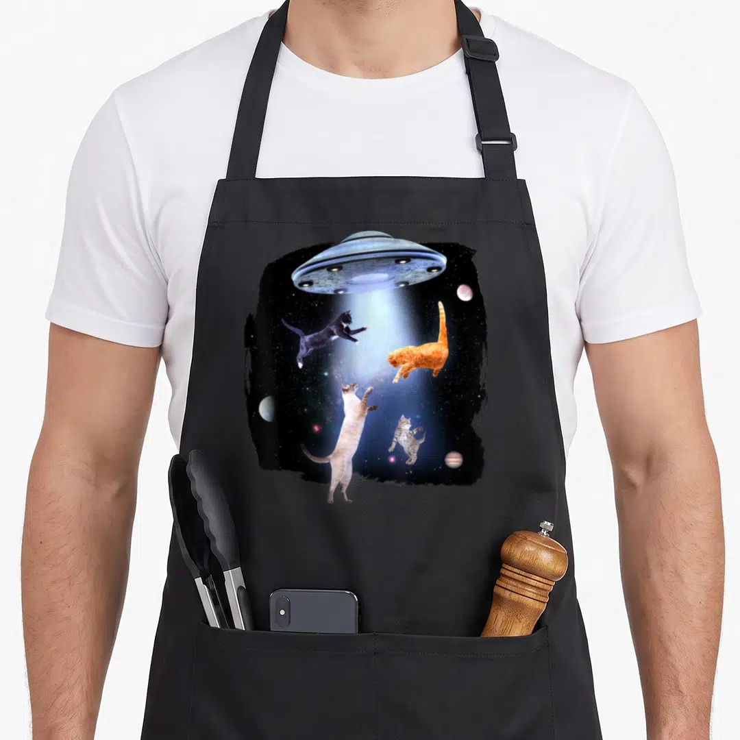 Kitty space cat apron - Four cats floating in a UFO beam with planets inside a rough black border — shown on a black cotton canvas apron against a white background