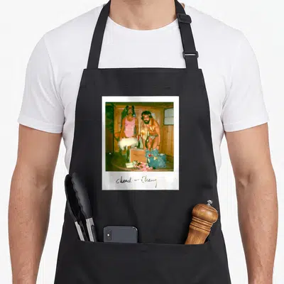 Chong chicha apron - Polaroid photo of two men in costumes with handwritten Cheech + Chong text below — shown on a black cotton canvas apron against a white background