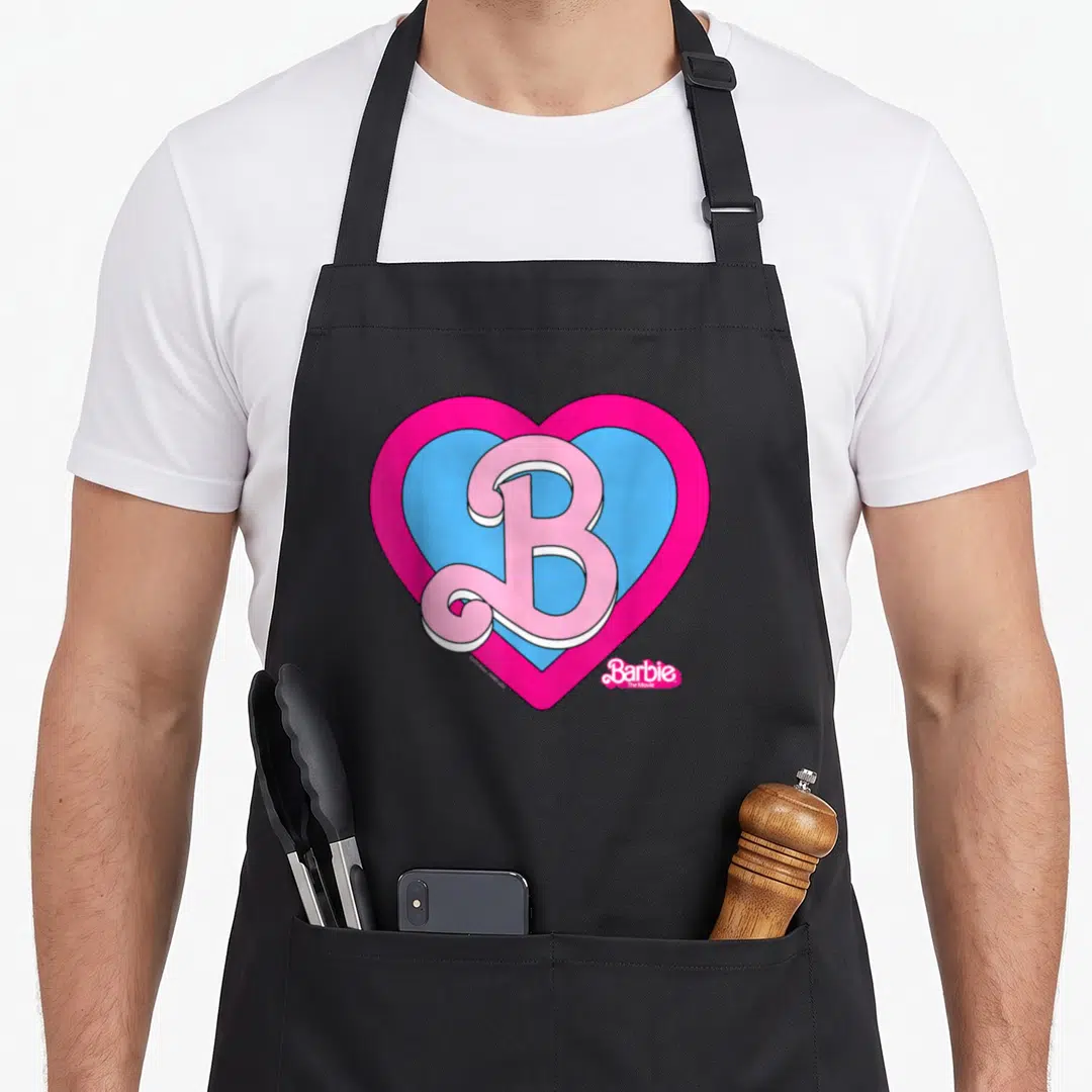 Movie barbiecore apron - Pink cursive B inside blue and pink hearts with white outlines and movie title text — shown on a black cotton canvas apron against a white background