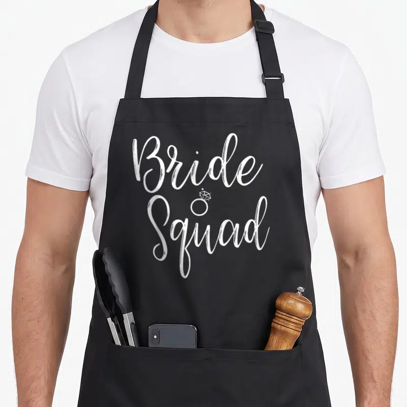 Squad bridal apron - White Bride Squad script text with small diamond ring icon between lines — shown on a black cotton canvas apron against a white background