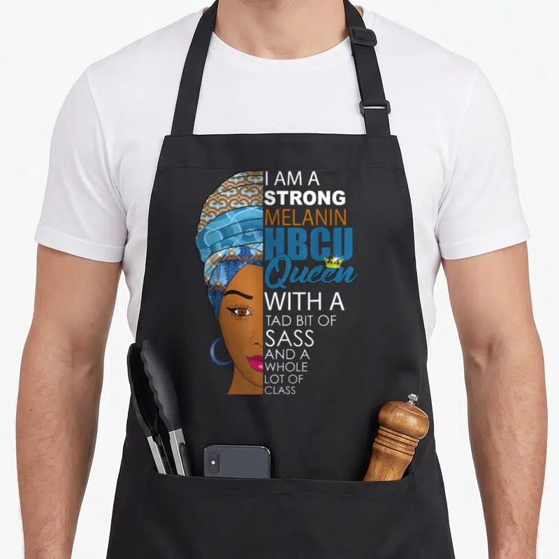 Grad queen apron - Woman's profile with patterned headwrap and stacked text reading I AM A STRONG MELANIN HBCU QUEEN — shown on a black cotton canvas apron against a white background