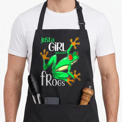 Retro frog aprons - Green cartoon frog with orange feet and text just a GIRL WHO LOVES fROGS — shown on a black cotton canvas apron against a white background