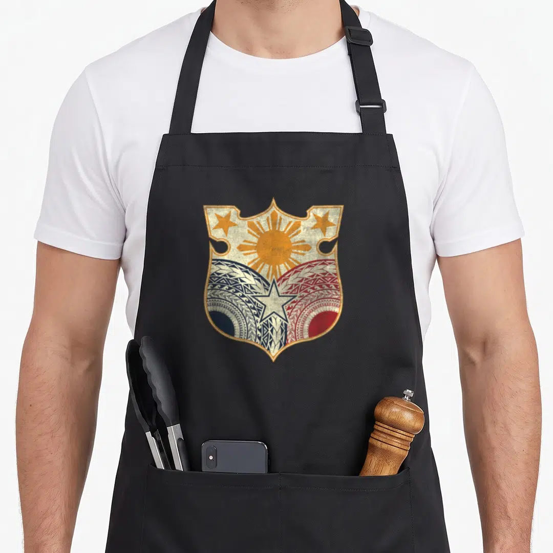 Filipino heritage aprons - Shield with sun, three stars, blue and red tribal patterns in gold and white — shown on a black cotton canvas apron against a white background
