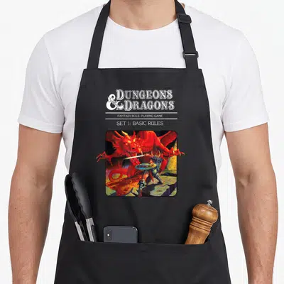 Rule basic apron - Stacked white text above red dragon fighting warrior in rounded frame — shown on a black cotton canvas apron against a white background