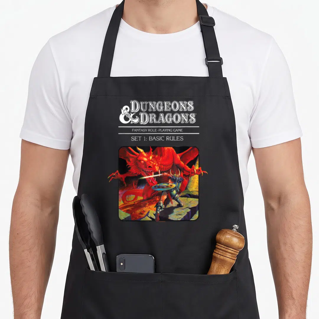 Rule basic apron - Stacked white text above red dragon fighting warrior in rounded frame — shown on a black cotton canvas apron against a white background