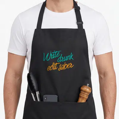 Drunk edit apron - Teal and orange text reading Write drunk edit sober on a dark background — shown on a black cotton canvas apron against a white background