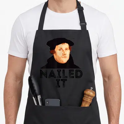 Martin nailed it aprons - Retro portrait of Martin Luther above stacked NAILED IT text in black and peach on grey — shown on a black cotton canvas apron against a white background