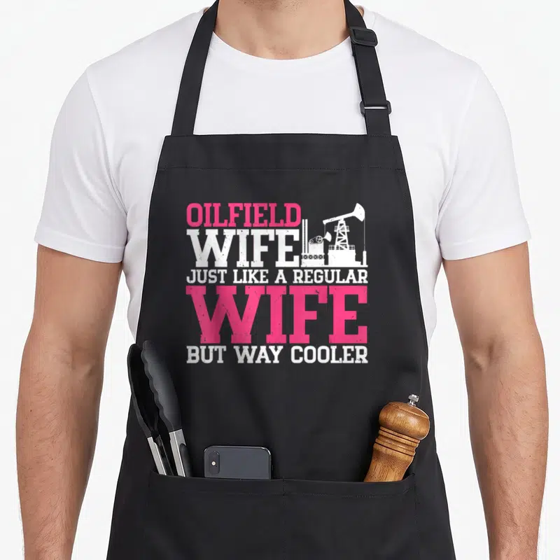 Coarse wife apron - Pink and white stacked text reading Oilfield Wife next to a white oil pump jack silhouette — shown on a black cotton canvas apron against a white background