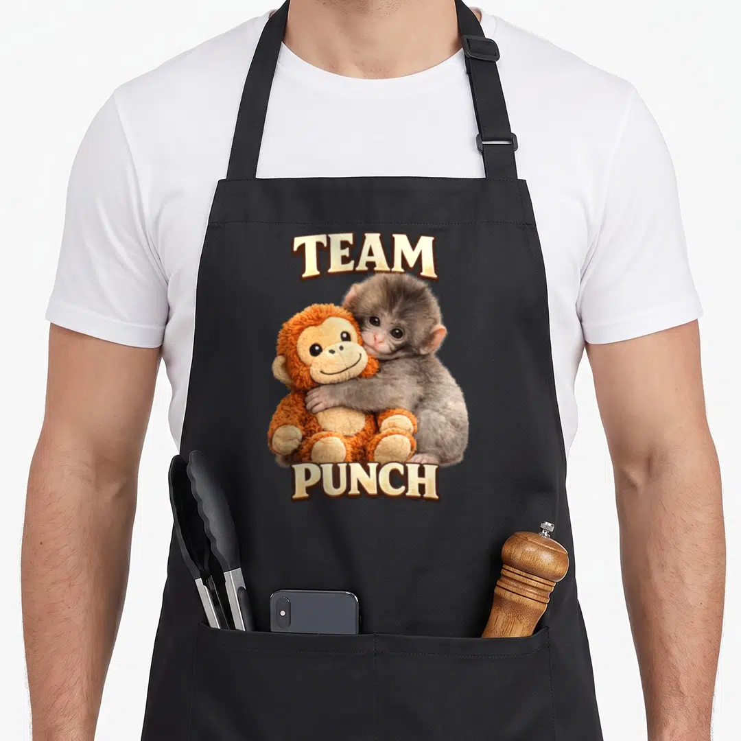 Punch monkey apron - Grey monkey hugging orange stuffed toy with team punch text — shown on a black cotton canvas apron against a white background