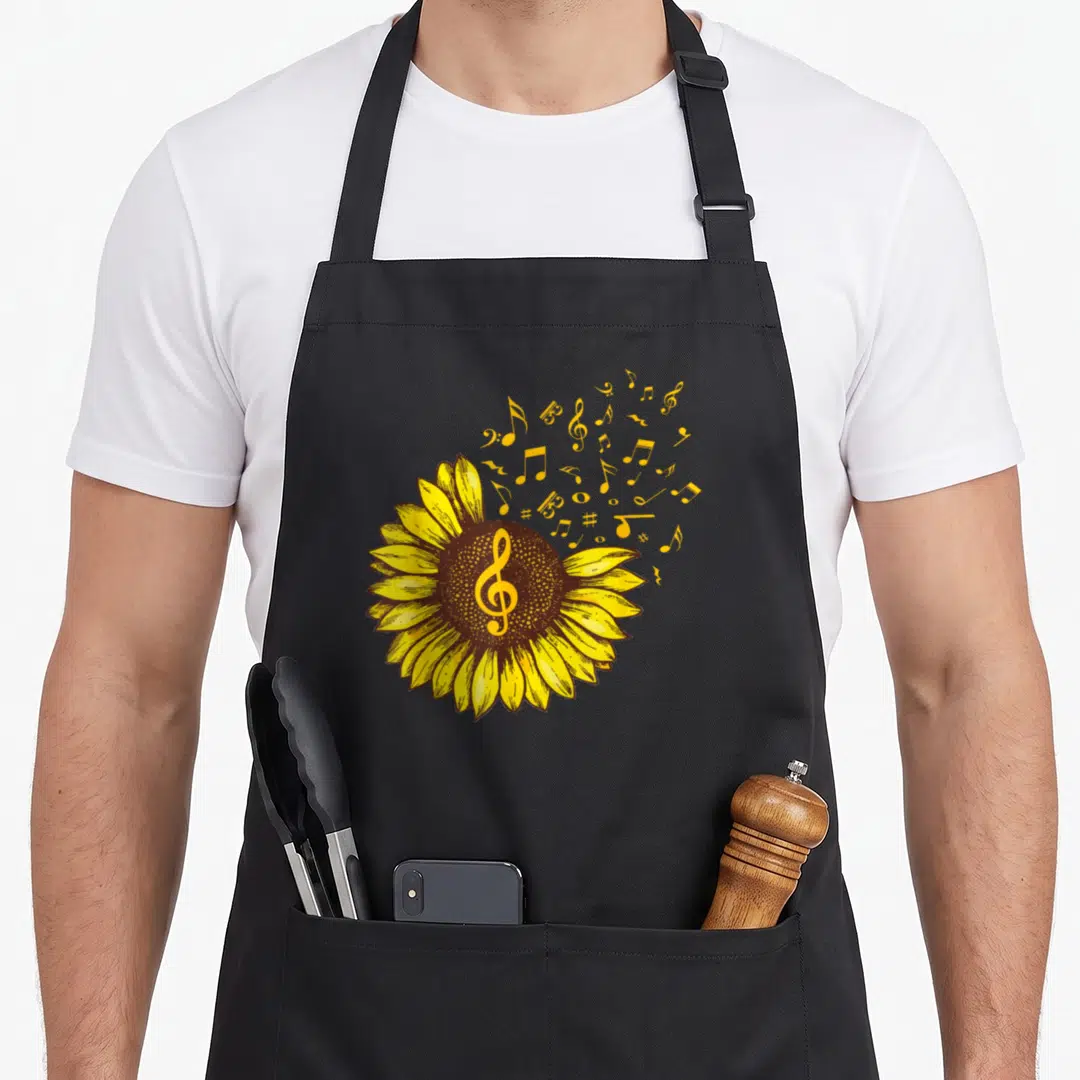 Music sunflower apron - Yellow sunflower with treble clef center and floating musical notes in cartoon style — shown on a black cotton canvas apron against a white background