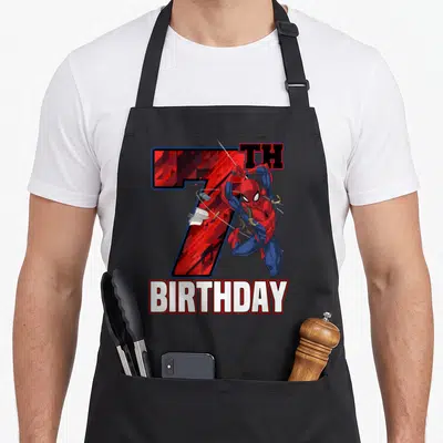 Web swing birthday apron - Spider-Man leaping in front of red 7TH BIRTHDAY text in cartoon style — shown on a black cotton canvas apron against a white background