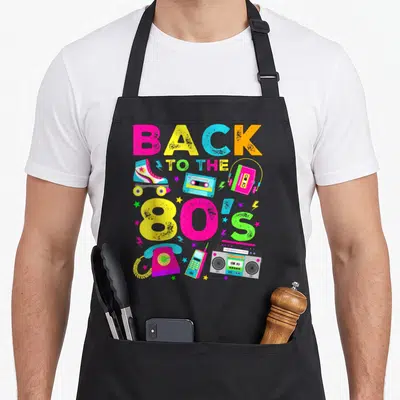 Funny eighty 80s apron - Stacked BACK TO THE 80'S text with roller skate, boombox, cassette, rotary phone in pink — shown on a black cotton canvas apron against a white background